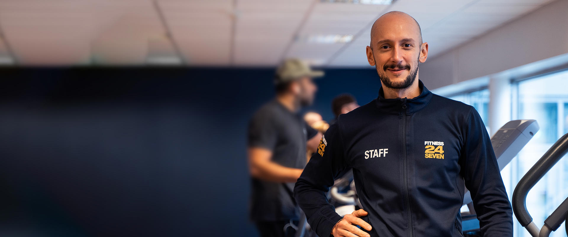 Personal på Fitness24Seven står på gymmet med cardio maskiner bakom